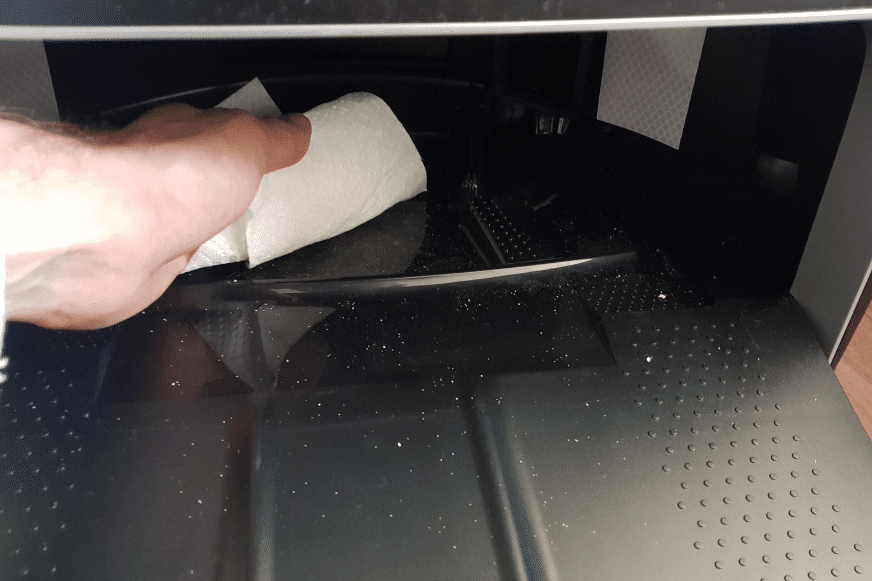 The floor of the wiping station is cleaned with a paper towel.